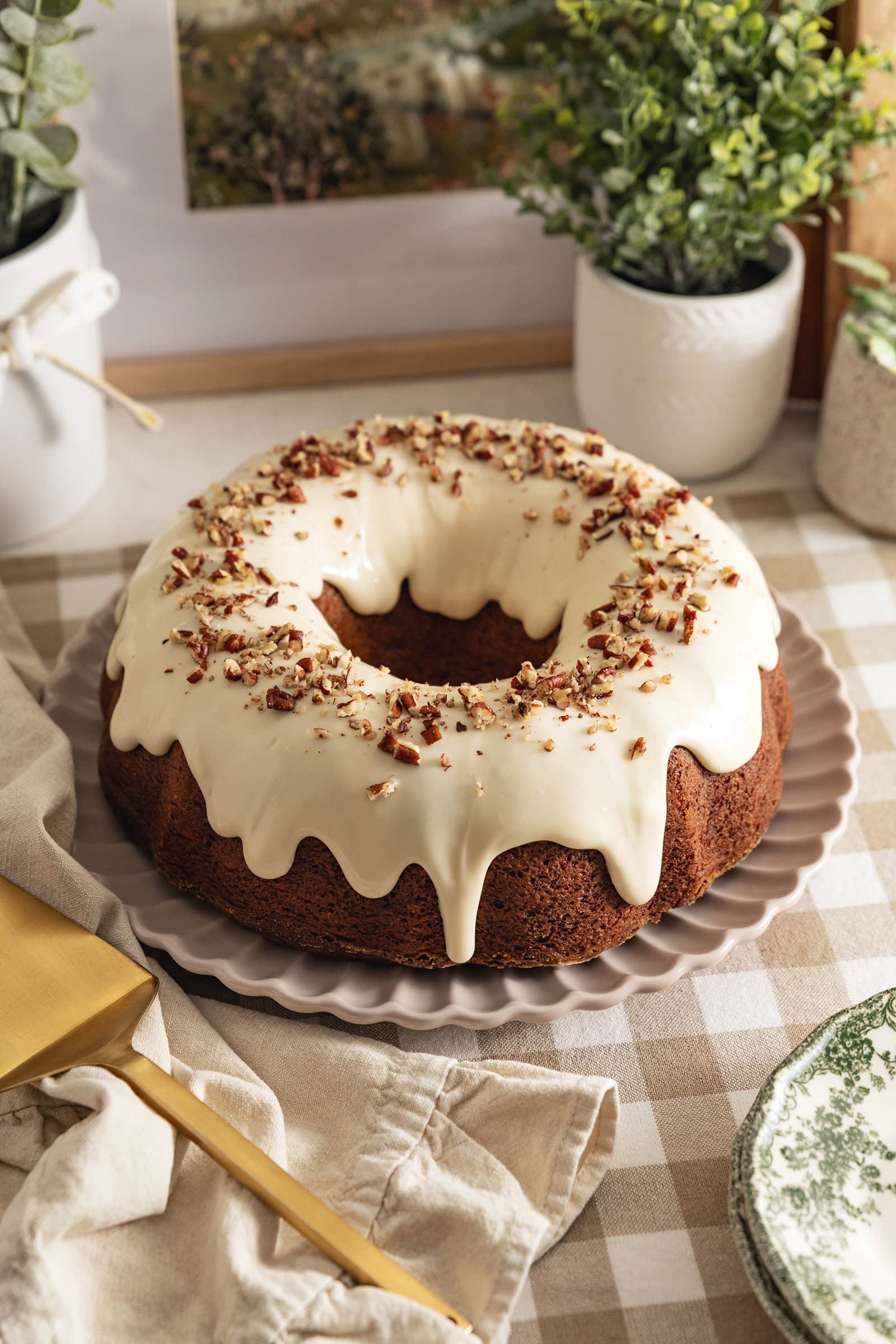 A carrot bundt cake with cream cheese frosting dripping down the sides on a kitchen counter.