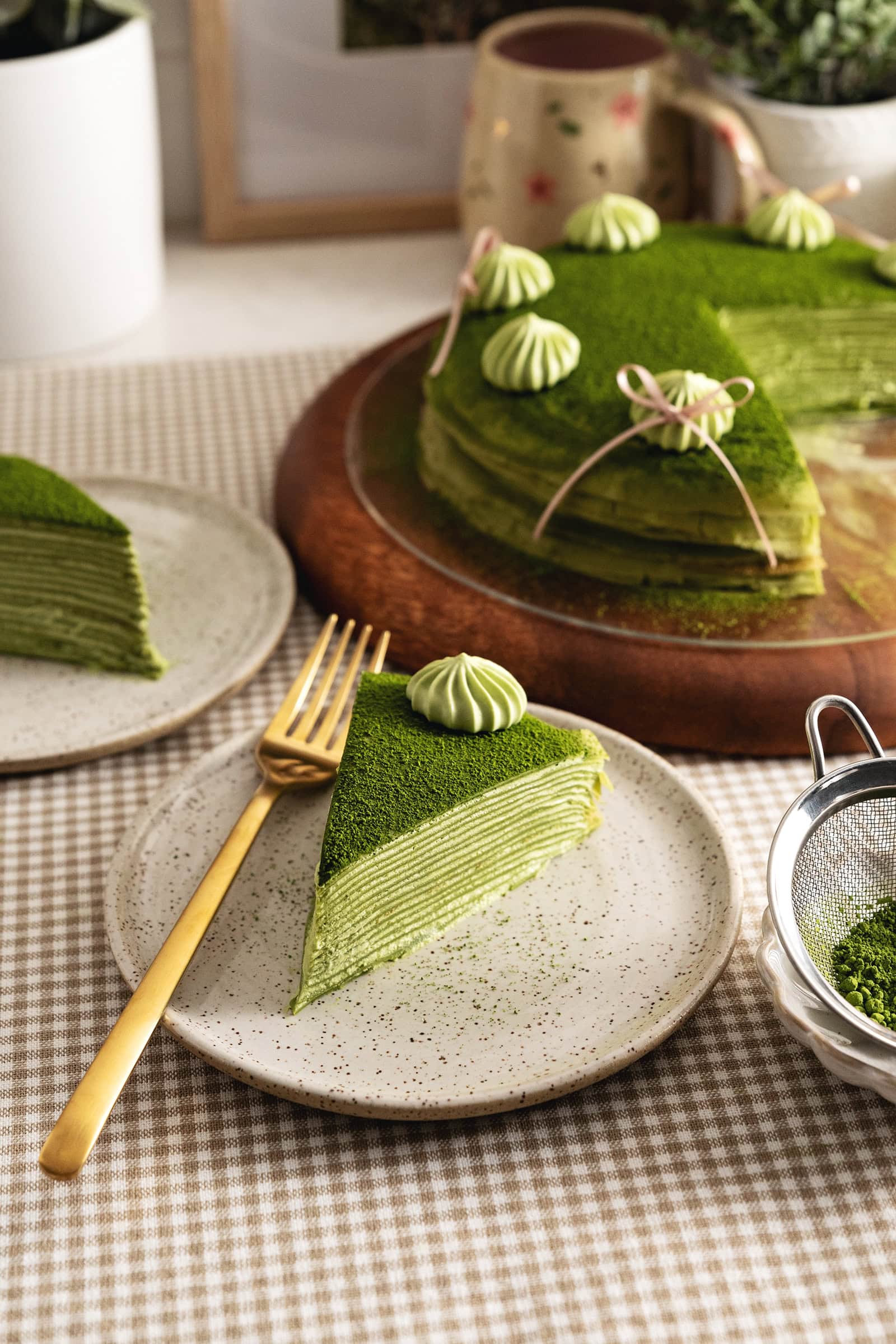 A slice of matcha mille crepe cake on a plate with a fork in front of the rest of the crepe cake.