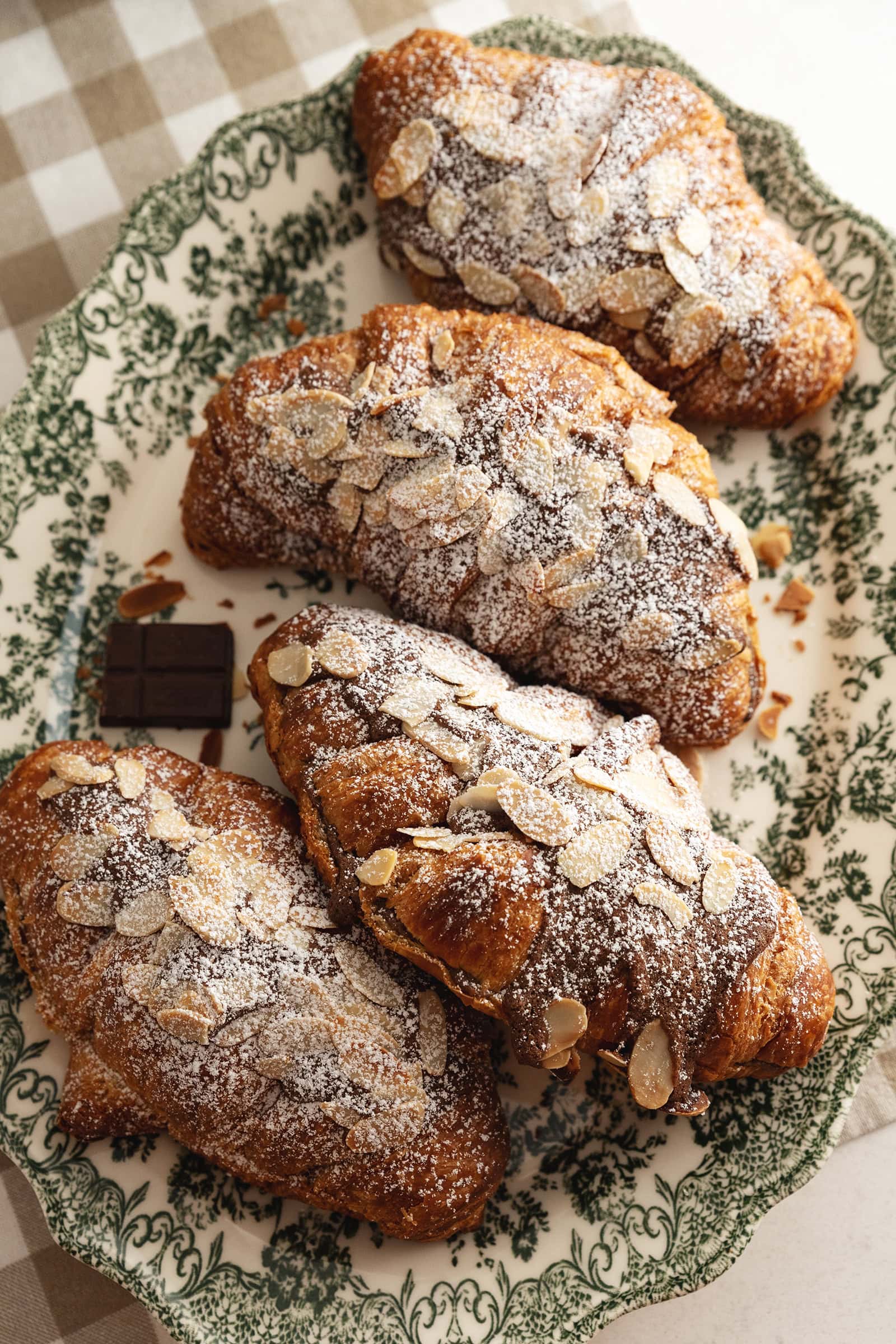 Four chocolate almond croissants on a green vintage serving plate.