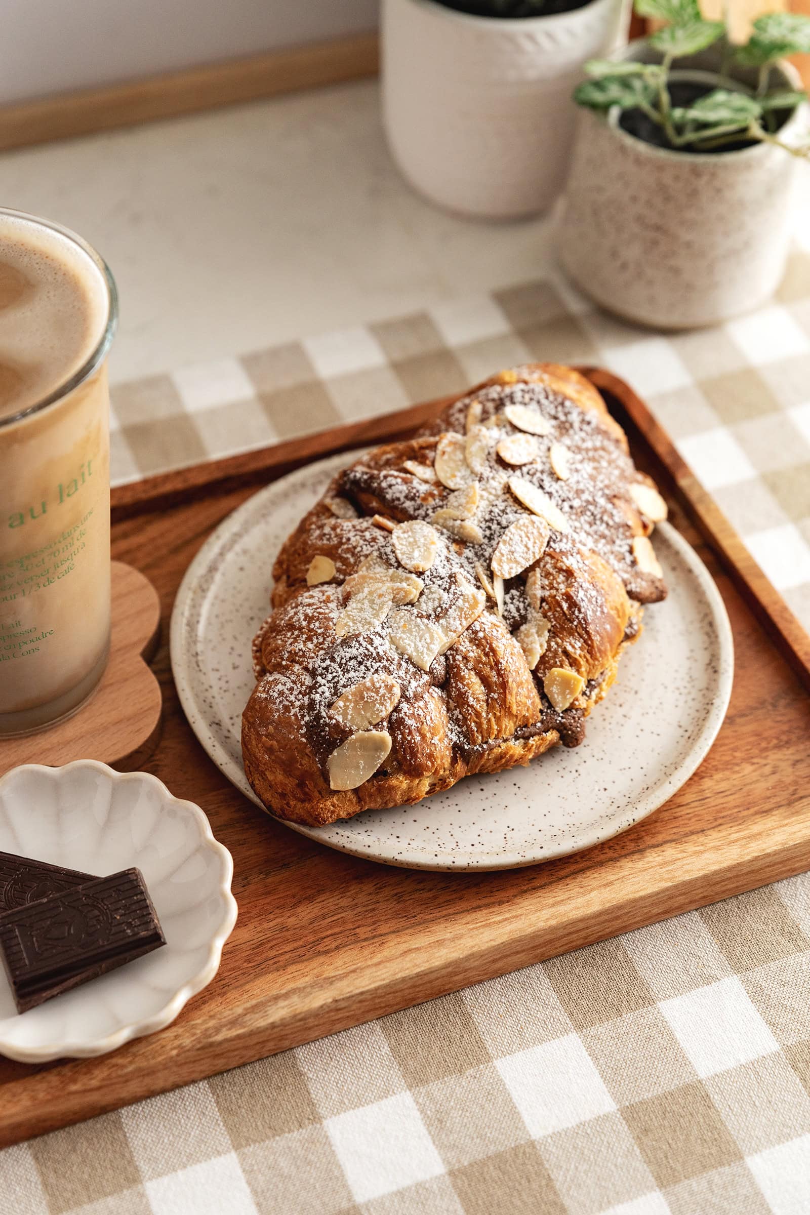 A chocolate almond croissant on a plate on a wood serving tray.