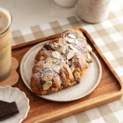 A chocolate almond croissant on a plate on a wood serving tray.