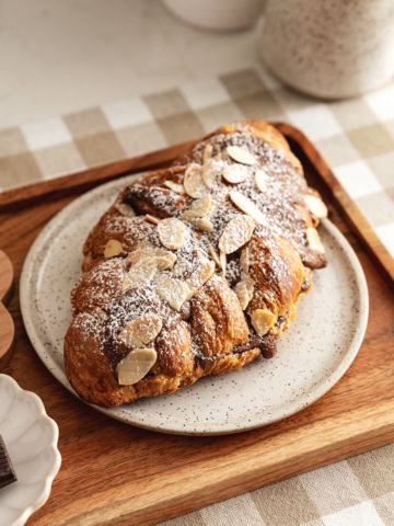 A chocolate almond croissant on a plate on a wood serving tray.