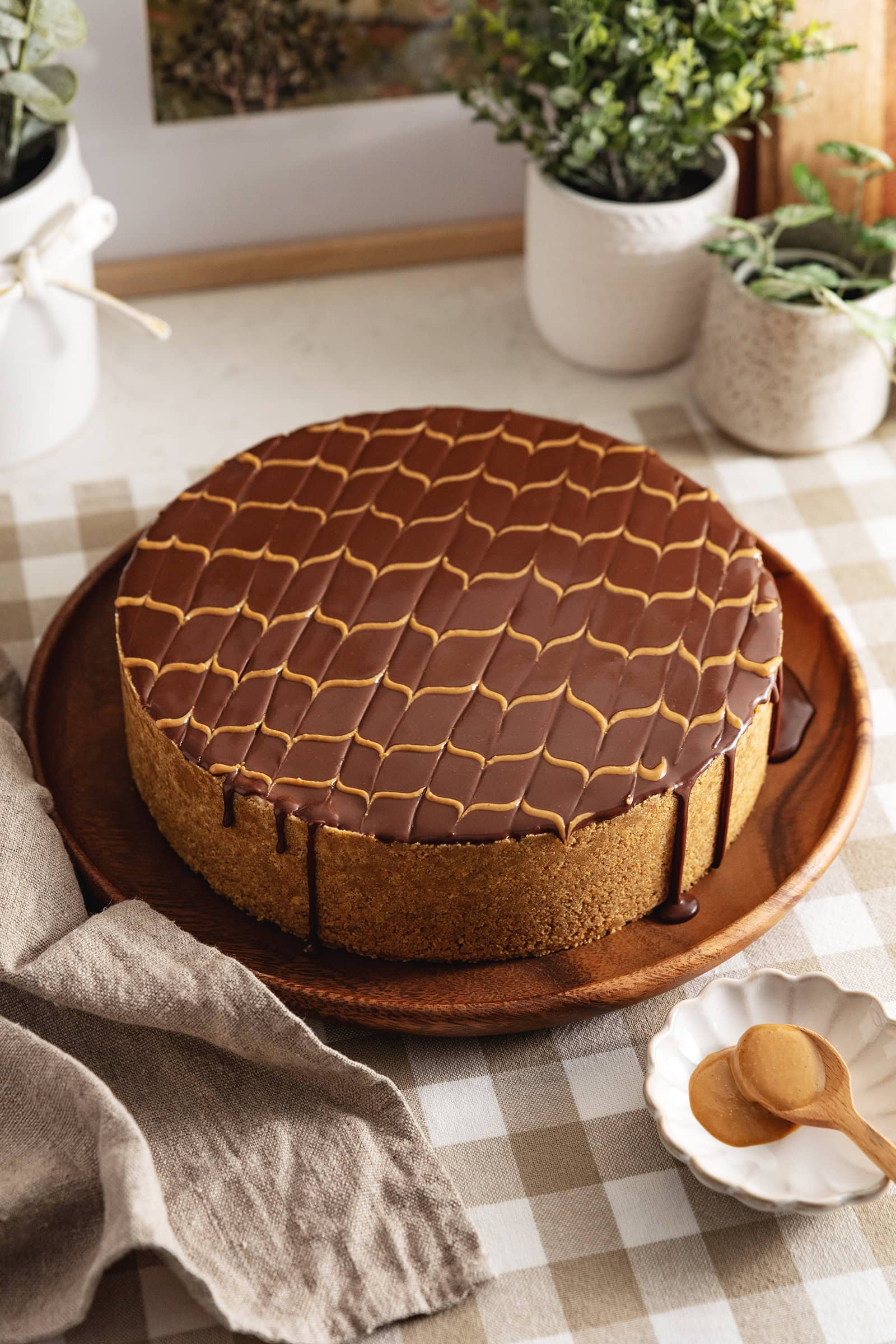 A chocolate peanut butter cheesecake with chocolate ganache dripping down the sides on a wooden platter.