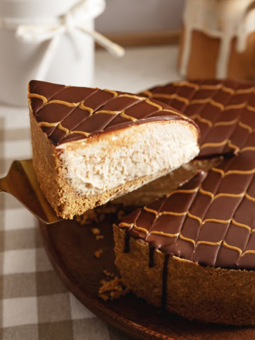 A slice of chocolate peanut butter cheesecake being lifted above the rest of the cake with a cake server.