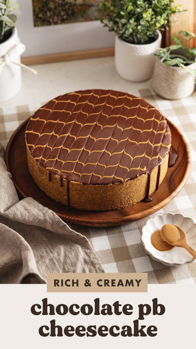 A chocolate peanut butter cheesecake with chocolate ganache dripping down the sides on a wooden platter.