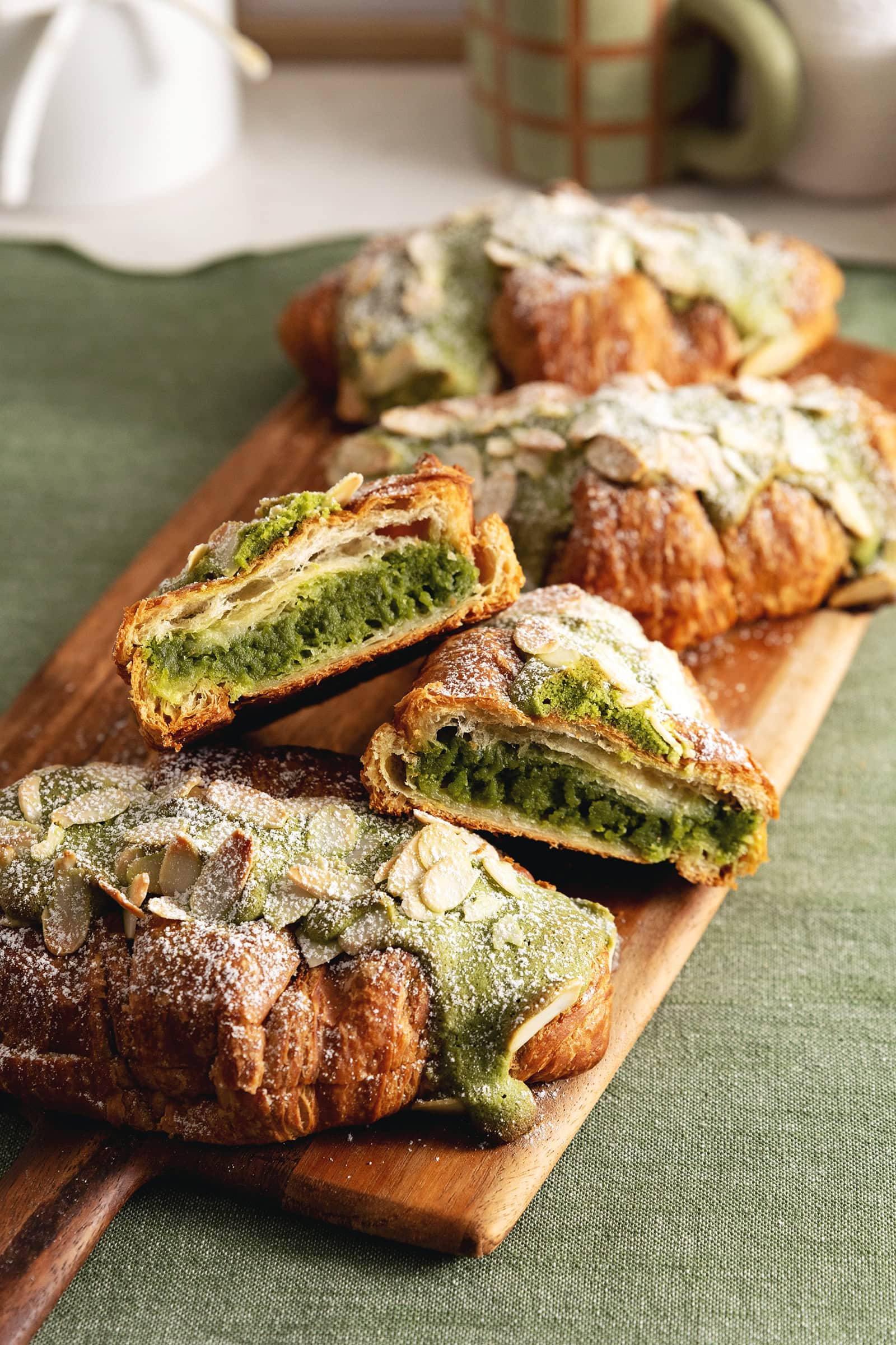 A matcha almond croissant cut in half to show the filling inside with other croissants on a wooden board.