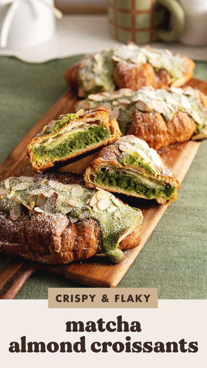 A matcha almond croissant cut in half to show the filling inside with other croissants on a wooden board.