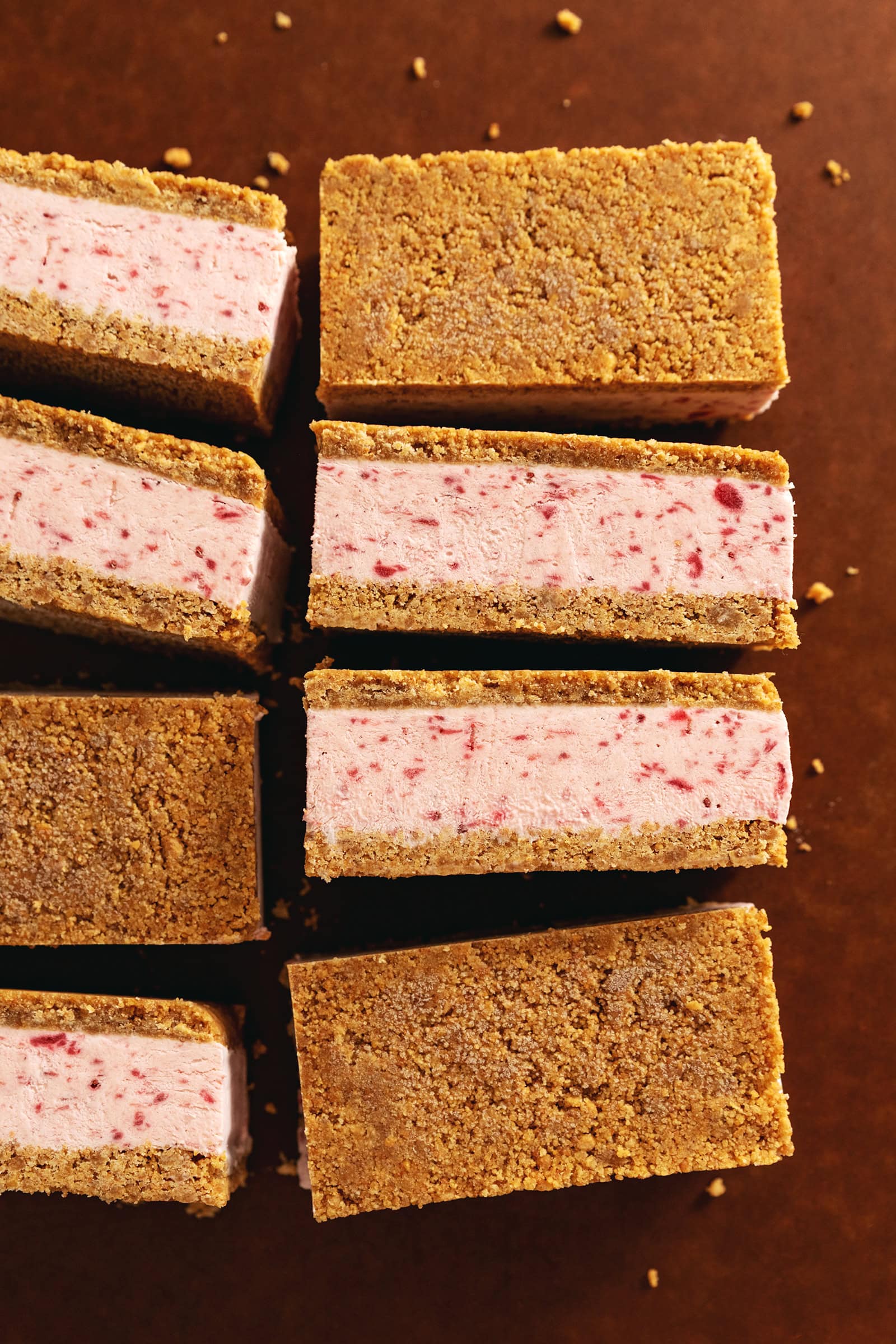 Strawberry ice cream sandwiches lined up on a wooden board showing the layers of ice cream and crust.