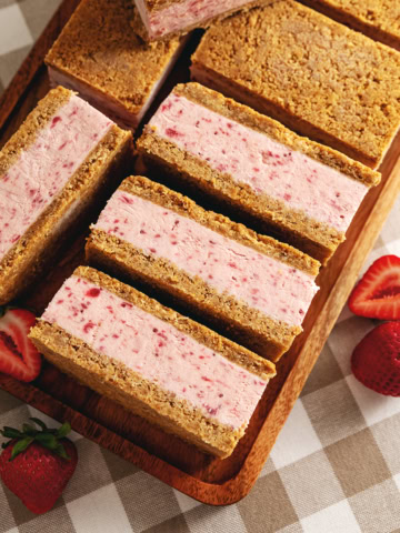 Strawberry ice cream sandwiches lined up on a wooden tray with fresh strawberries around it.