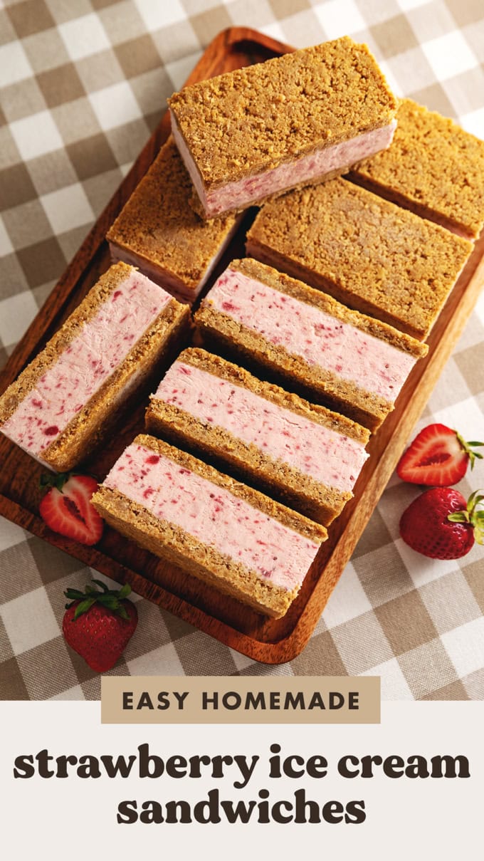 Strawberry ice cream sandwiches lined up on a wooden tray with fresh strawberries around it.