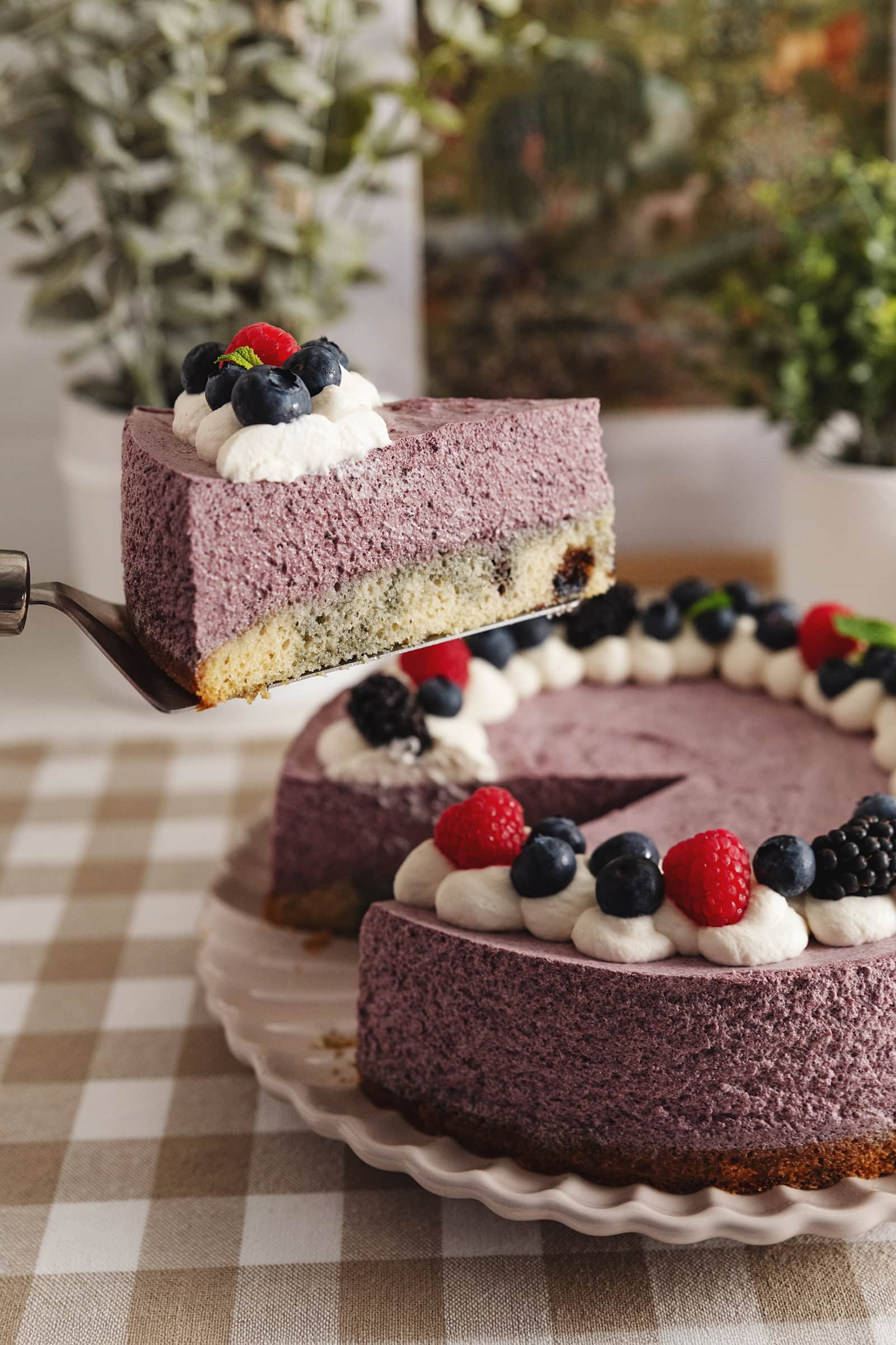 Lifting a slice of blueberry mousse cake above the rest of the cake with a cake server.