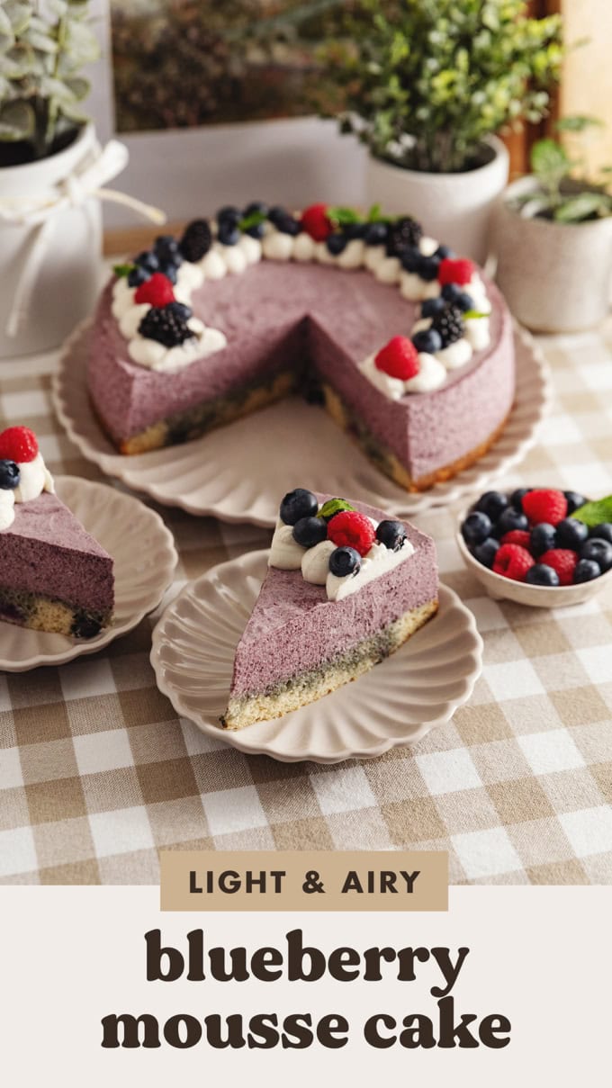 Two slices of blueberry mousse cake on plates in front of the rest of the cake on a kitchen counter.
