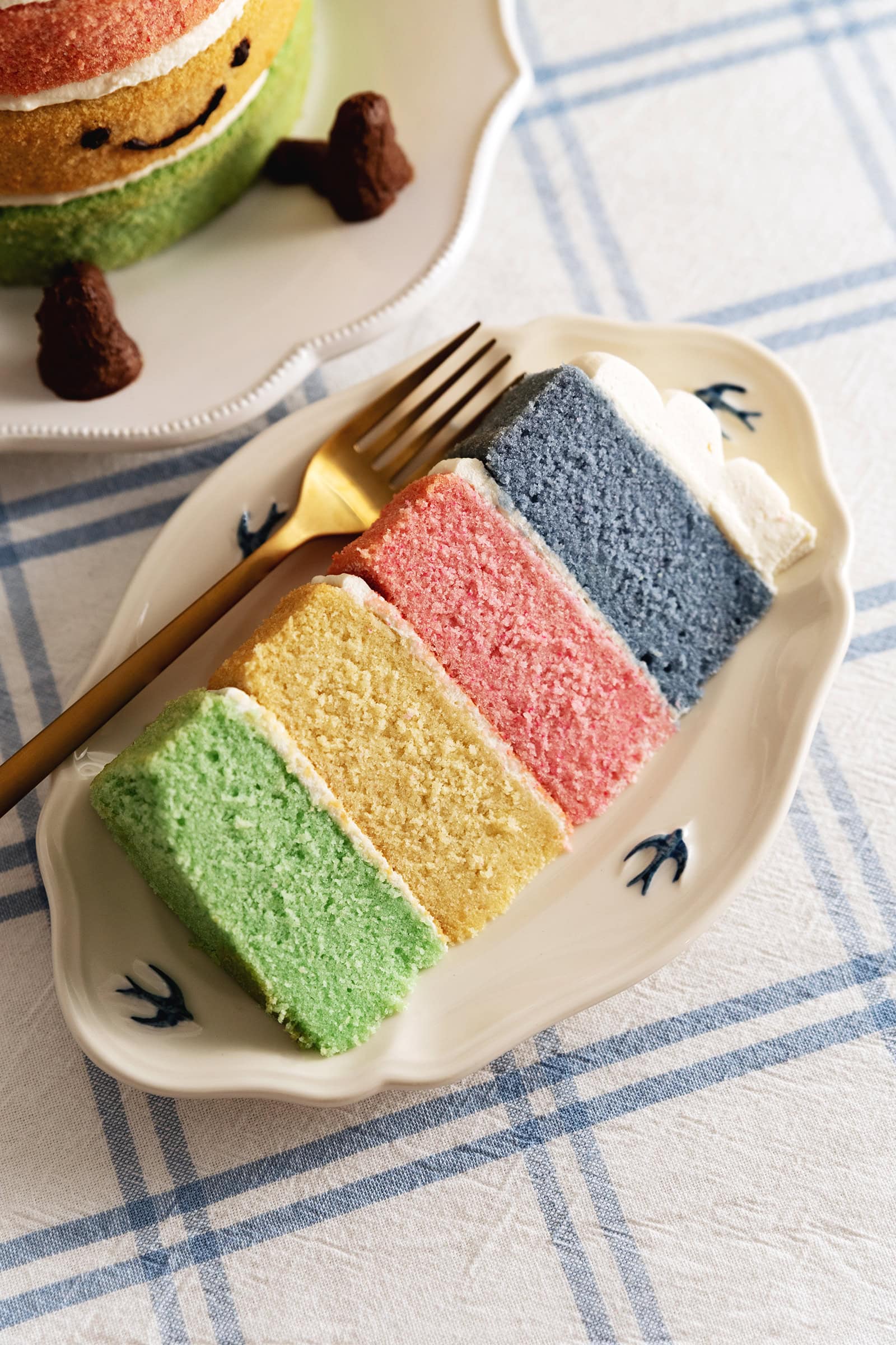 A slice of Jellycat rainbow cake on a plate with a fork.