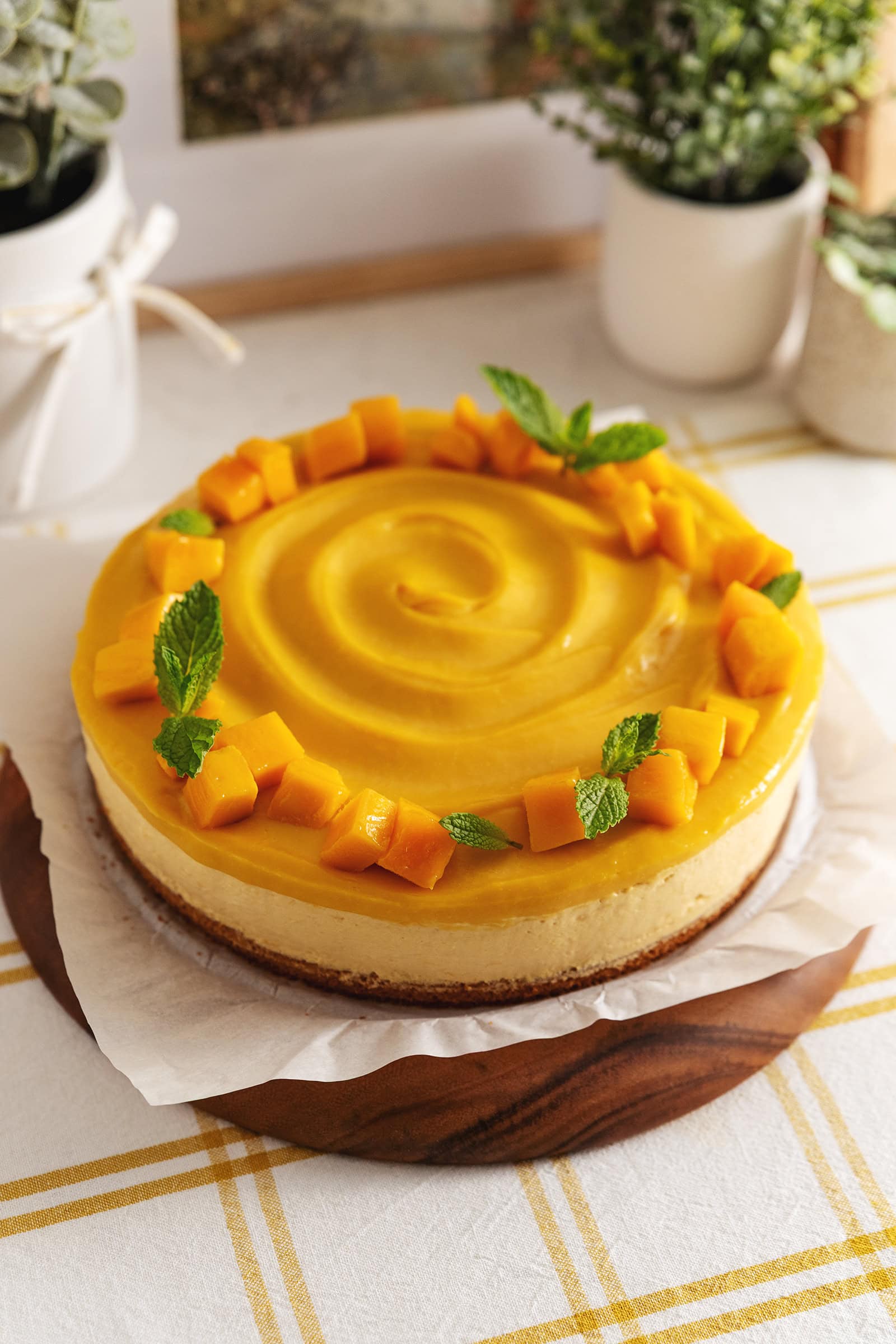 A mango mousse cake with mango chunks on top on a wooden platter.