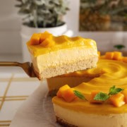 A slice of mango mousse cake being lifted above the rest of the cake to show the layers.