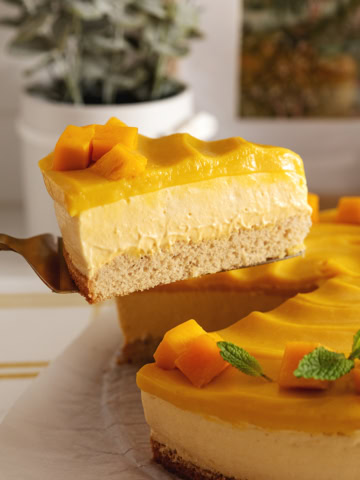 A slice of mango mousse cake being lifted above the rest of the cake to show the layers.