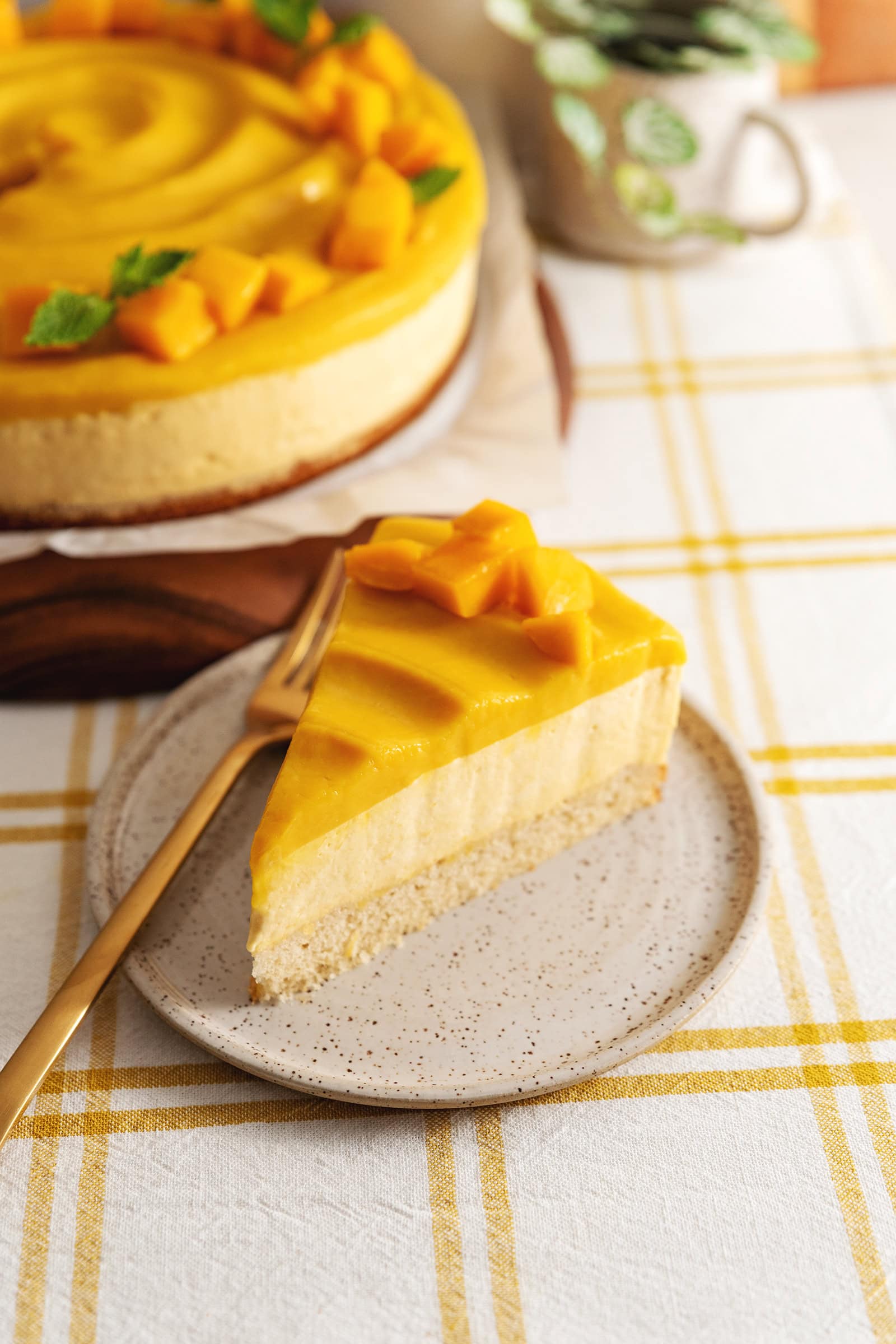 A slice of mango mousse cake on a plate in front of the rest of the cake.