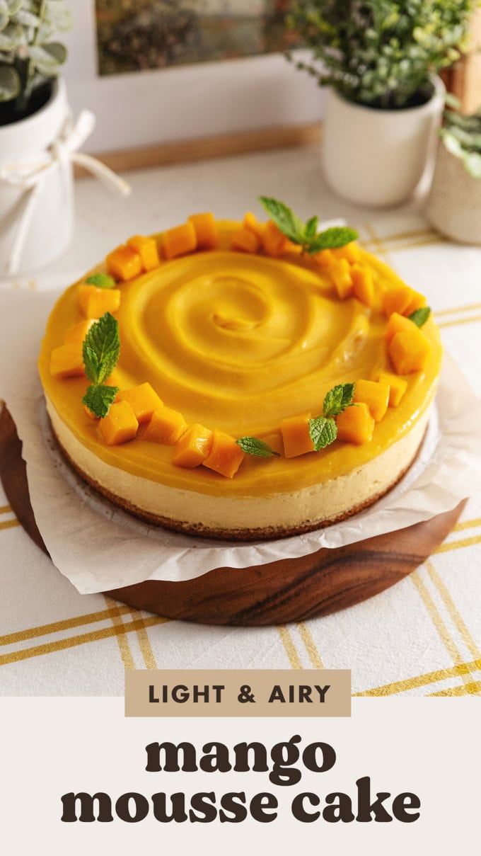 A mango mousse cake with mango chunks on top on a wooden platter.