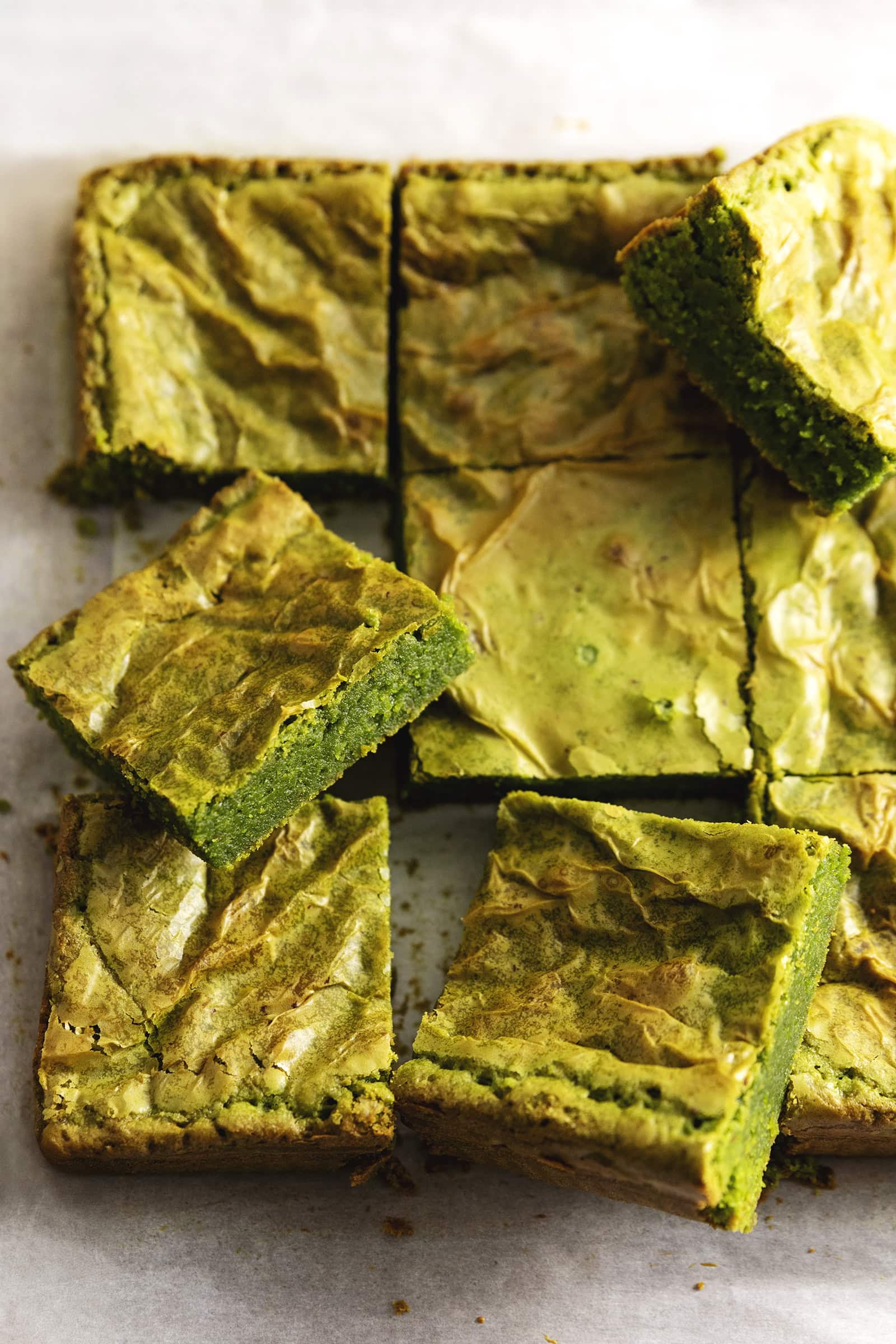 Matcha brownies on parchment paper with some brownies tilted and resting on the others.
