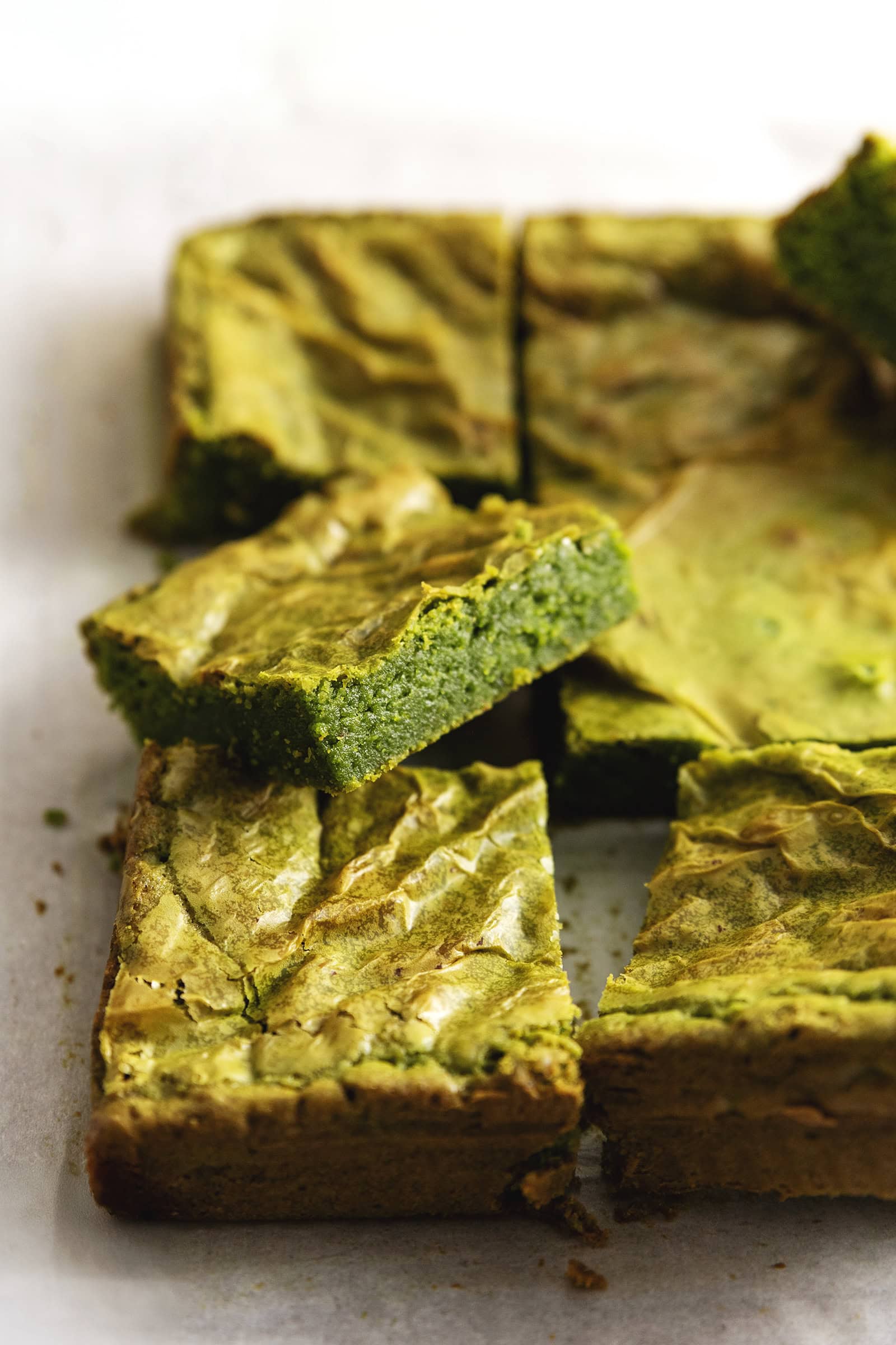 Close-up of a matcha brownie rest on other brownies on parchment paper.