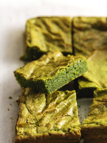 Close-up of a matcha brownie rest on other brownies on parchment paper.