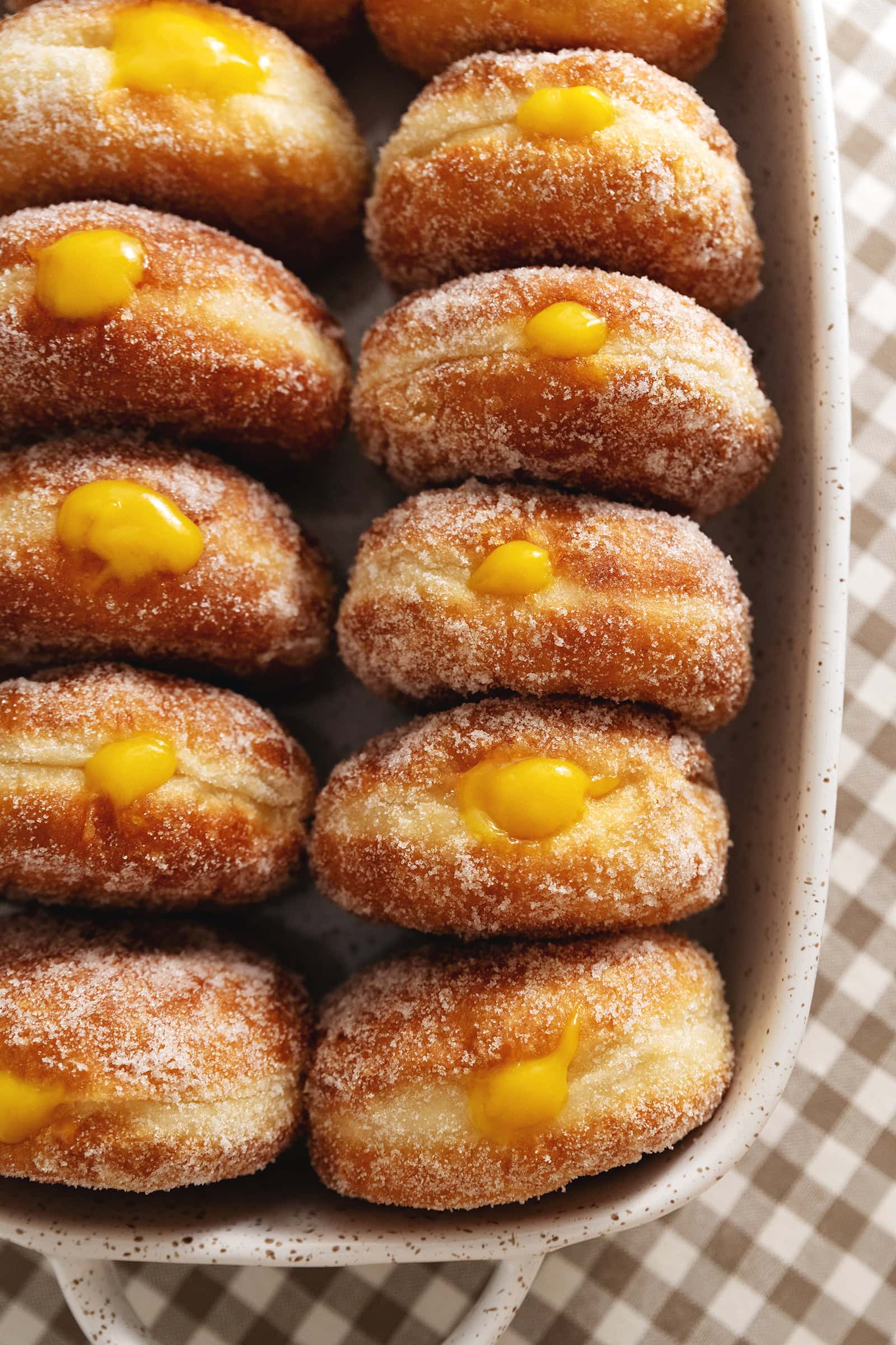 Several mango brioche donuts lined up in a baking dish with mango curd coming out of the tops of each donut.
