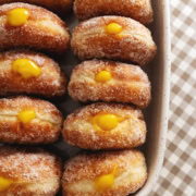 Several mango brioche donuts lined up in a baking dish with mango curd coming out of the tops of each donut.