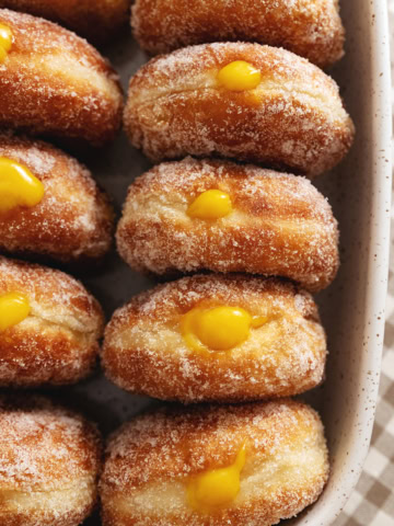 Several mango brioche donuts lined up in a baking dish with mango curd coming out of the tops of each donut.