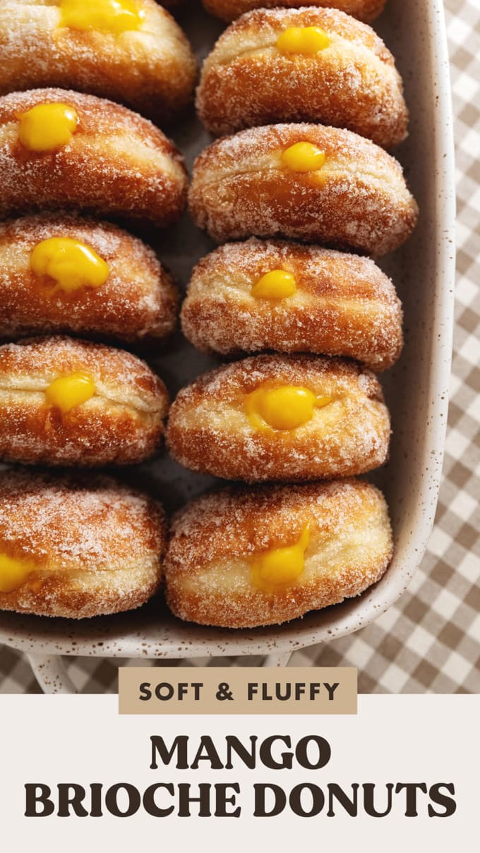 Several mango brioche donuts lined up in a baking dish with mango curd coming out of the tops of each donut.