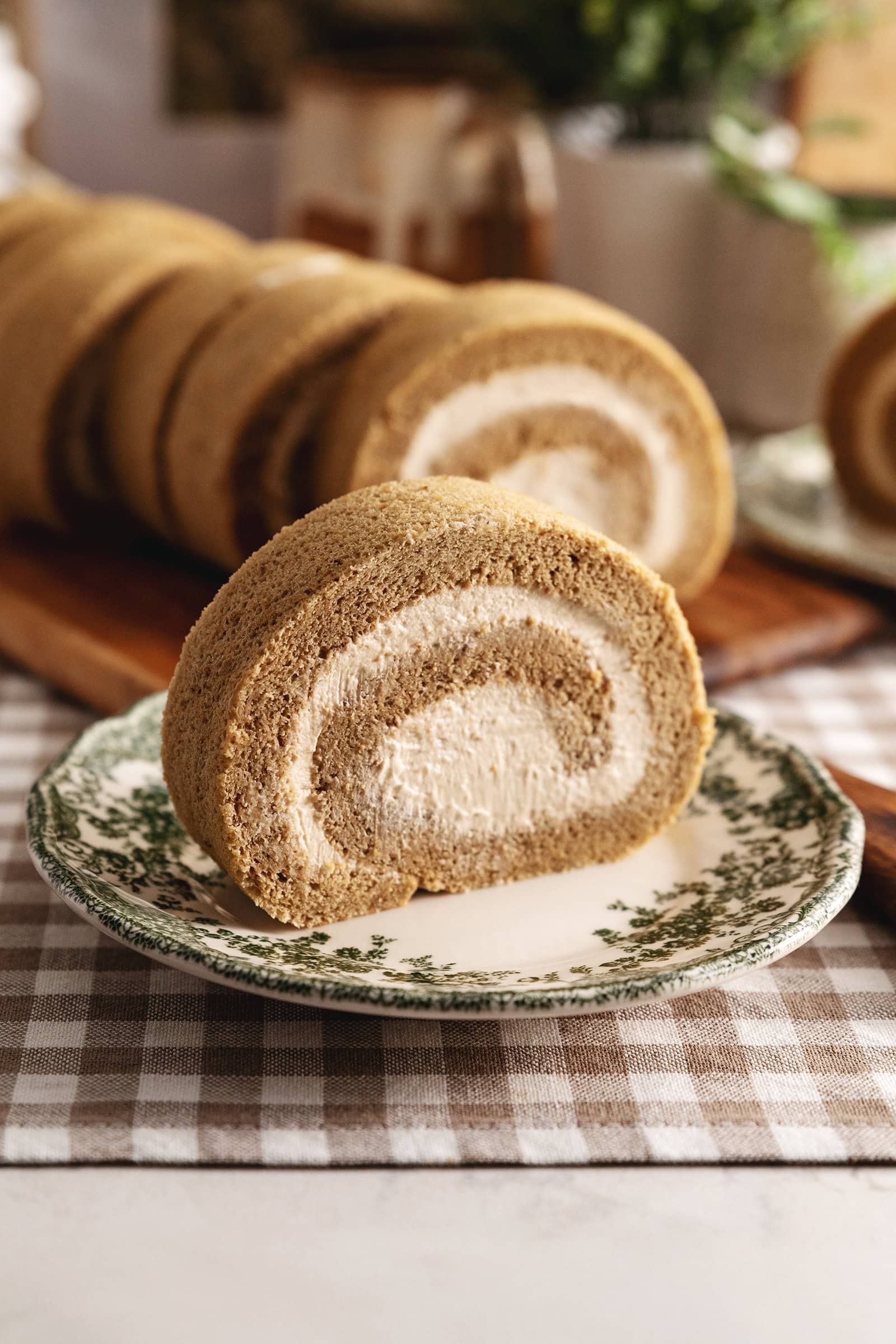 A slice of coffee swiss roll on a vintage plate with several other slices in the background.