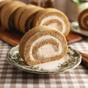 A slice of coffee swiss roll on a vintage plate with several other slices in the background.