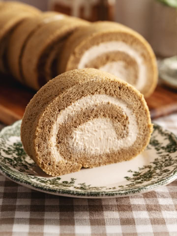A slice of coffee swiss roll on a vintage plate with several other slices in the background.