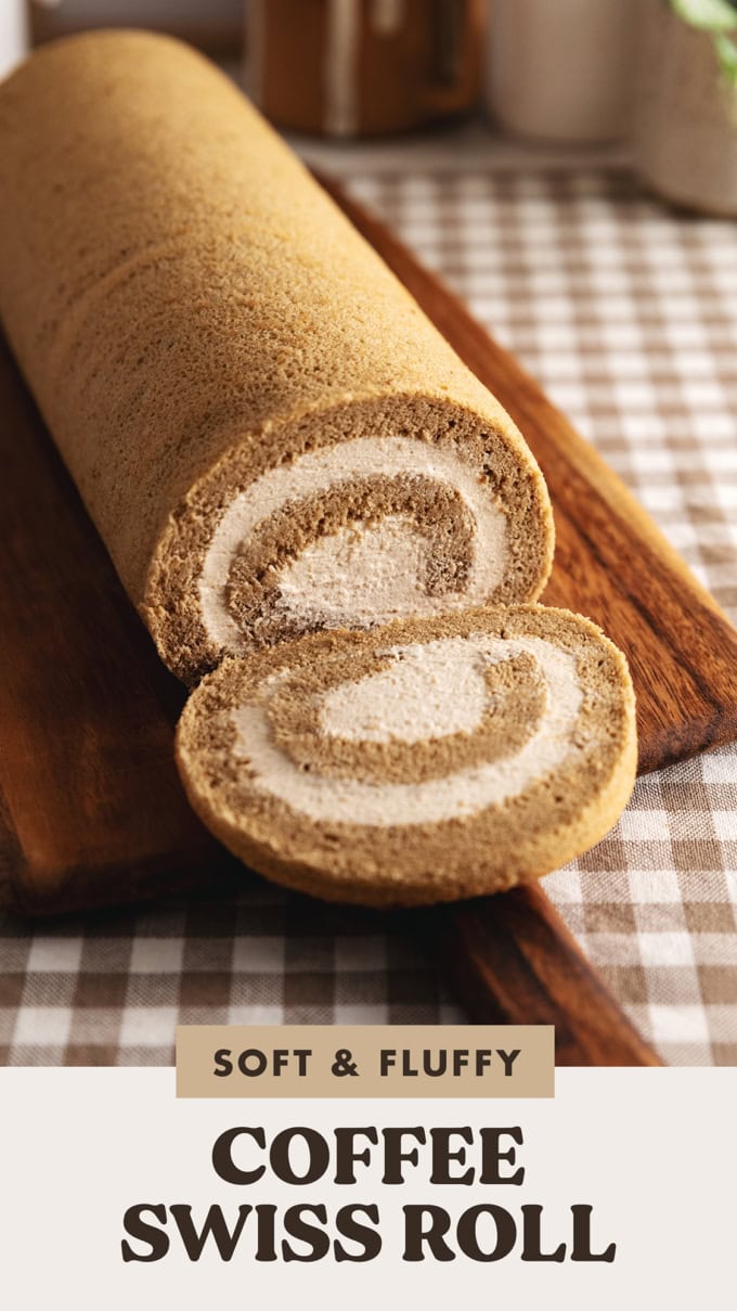 A coffee swiss roll on a wooden board with one slice cut and laying down in front of the rest of the cake.