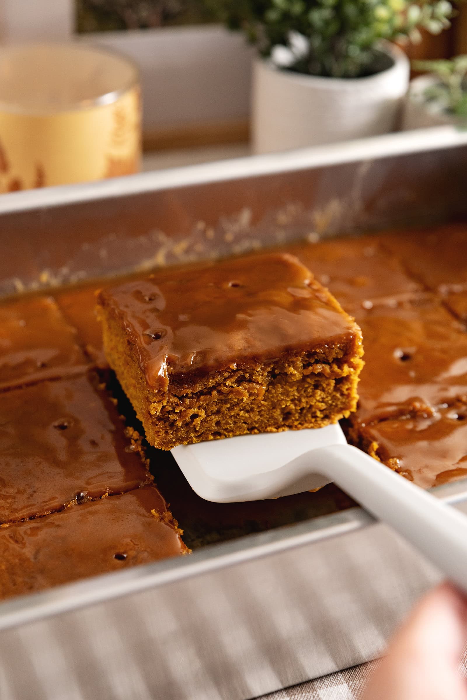 A square of pumpkin sticky toffee pudding being lifted from a baking tray with a spatula.