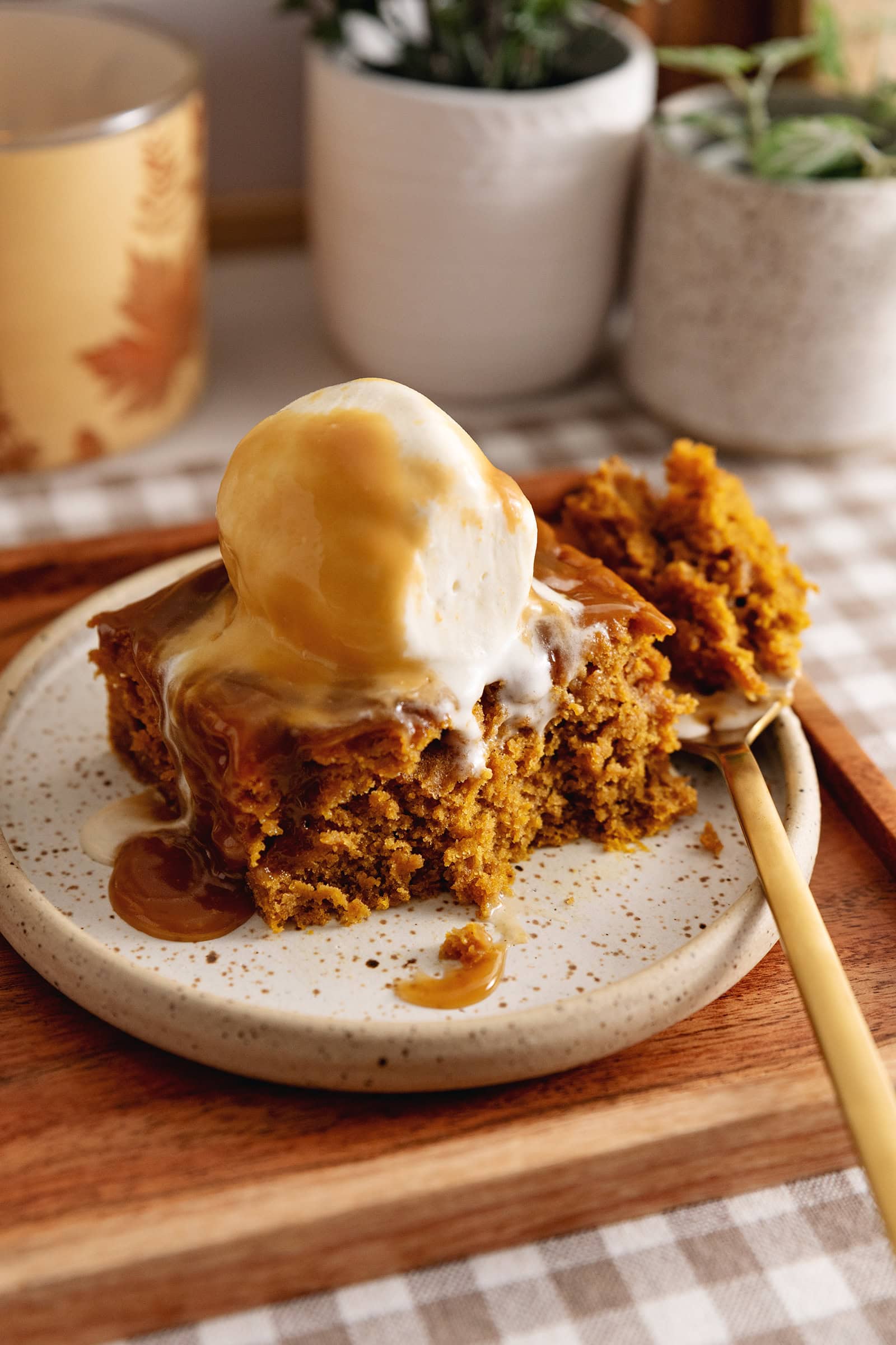 A slice of pumpkin sticky toffee pudding on a plate with a forkful taken out of it to show the cake texture.