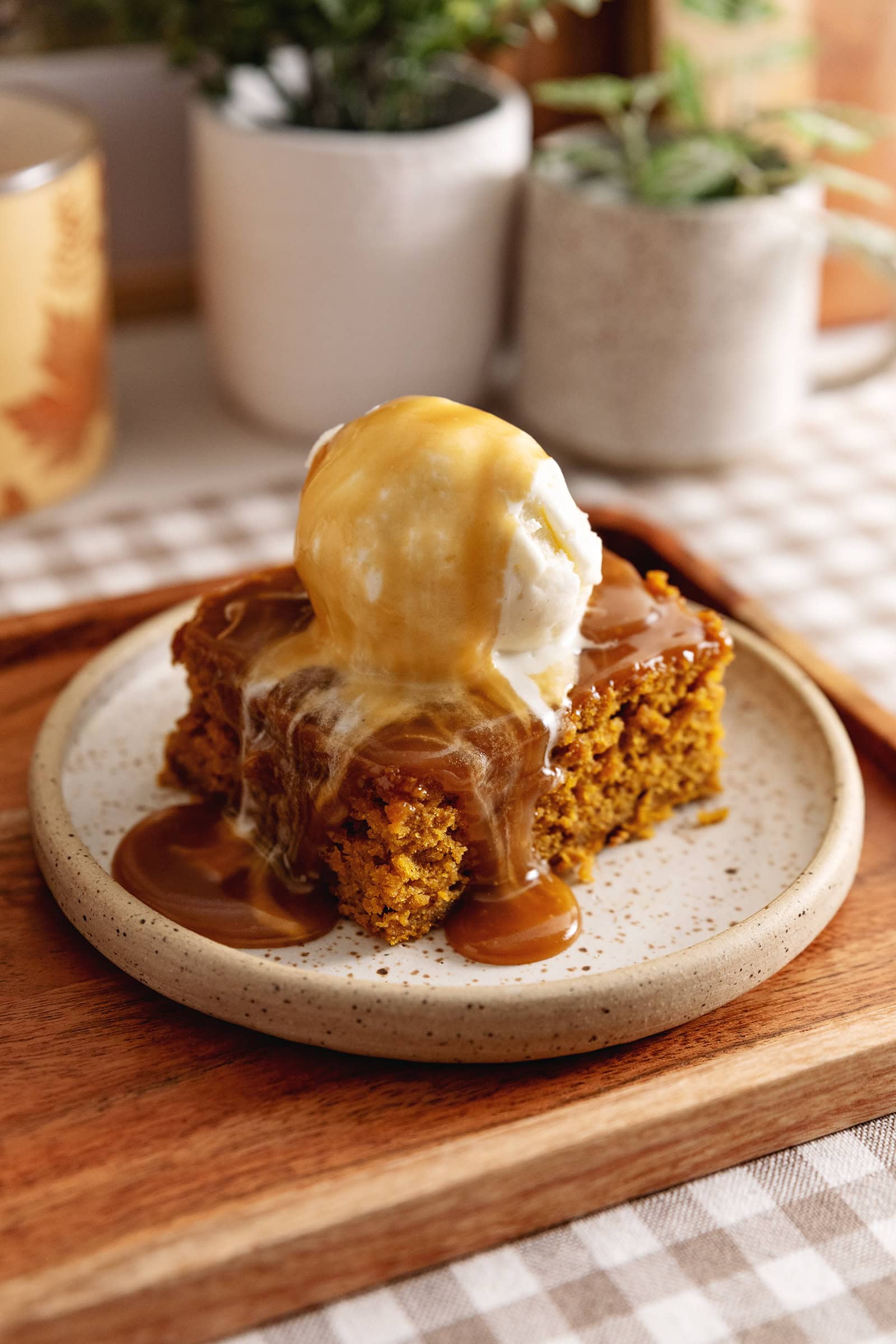 A slice of pumpkin sticky toffee pudding on a plate with a scoop of ice cream on top and toffee sauce dripping down.