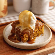 A slice of pumpkin sticky toffee pudding on a plate with a scoop of ice cream on top and toffee sauce dripping down.