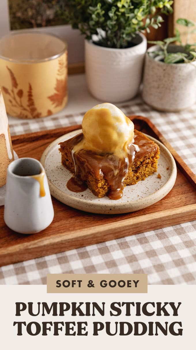 A slice of pumpkin sticky toffee pudding on a wooden tray with a small cup of toffee sauce next to it.