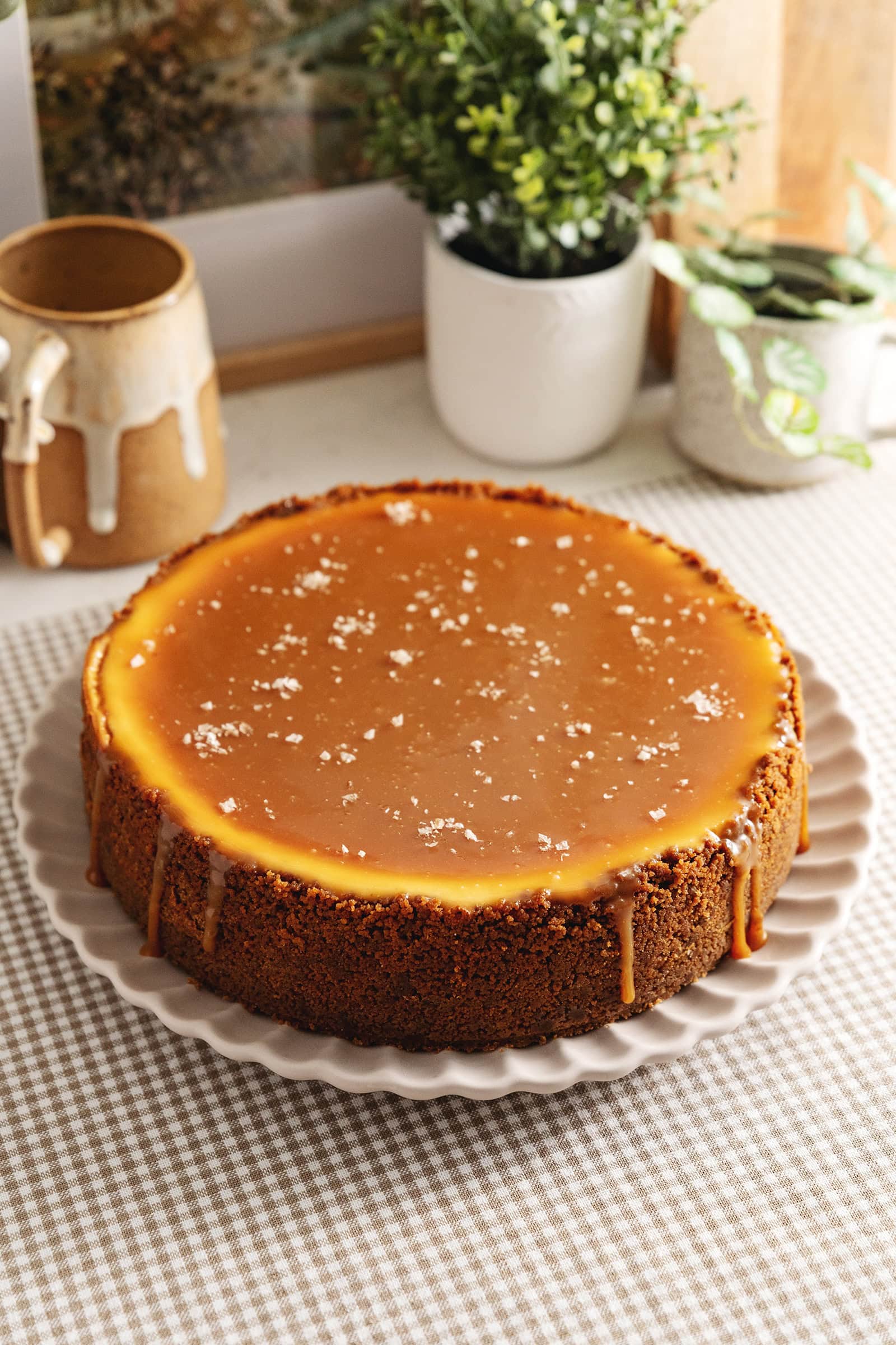 A salted caramel cheesecake on a plate with caramel dripping down the sides and flaky salt on top.