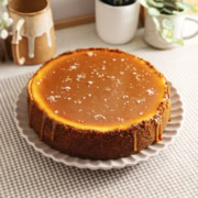 A salted caramel cheesecake on a plate with caramel dripping down the sides and flaky salt on top.