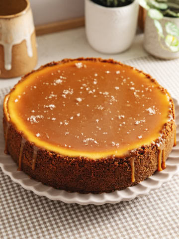 A salted caramel cheesecake on a plate with caramel dripping down the sides and flaky salt on top.