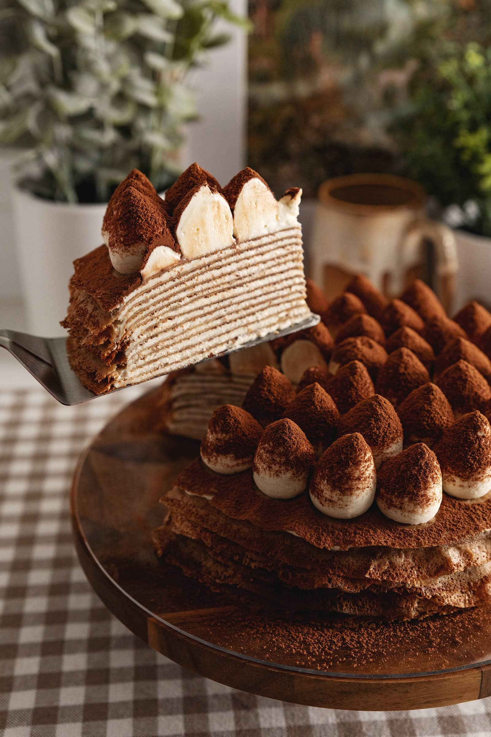 A slice of tiramisu crepe cake being lifted with a cake server from the rest of the cake to show the crepe layers inside.