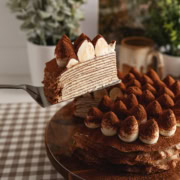A slice of tiramisu crepe cake being lifted with a cake server from the rest of the cake to show the crepe layers inside.