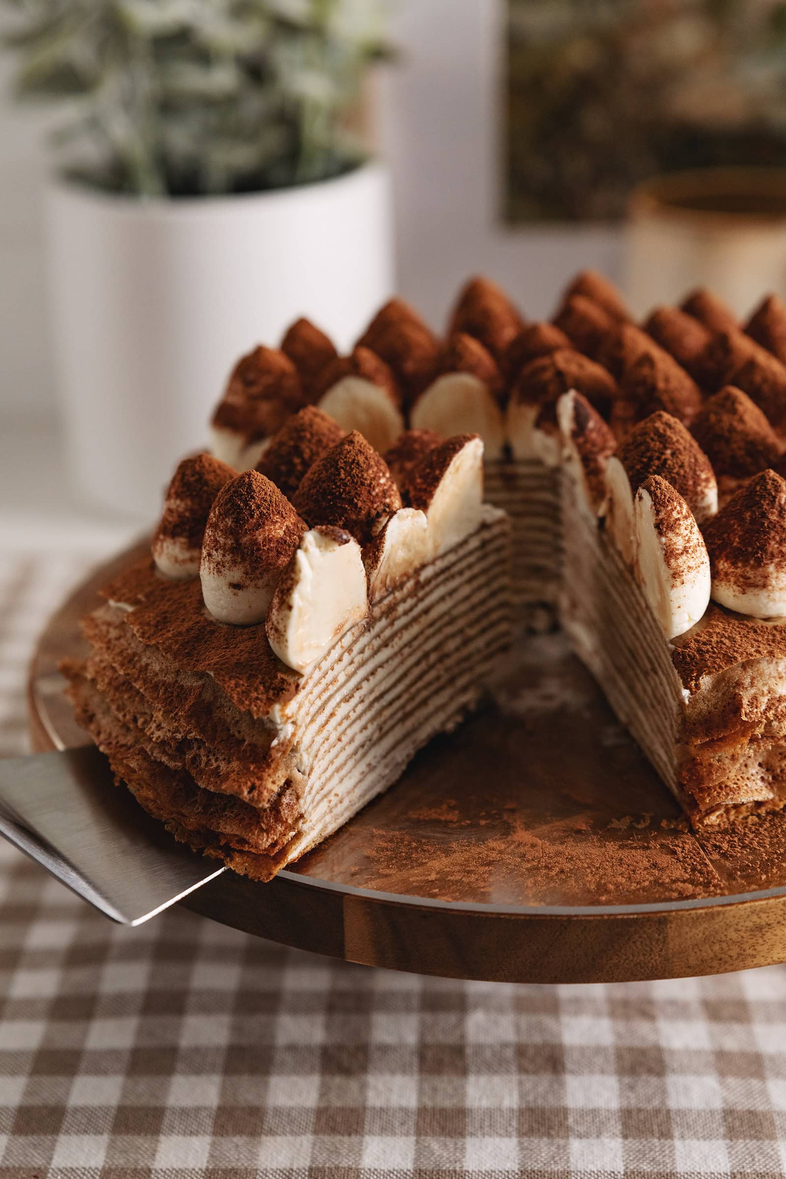 A slice of tiramisu crepe cake cut from the rest of the cake, sitting at an angle to show the crepe layers inside.