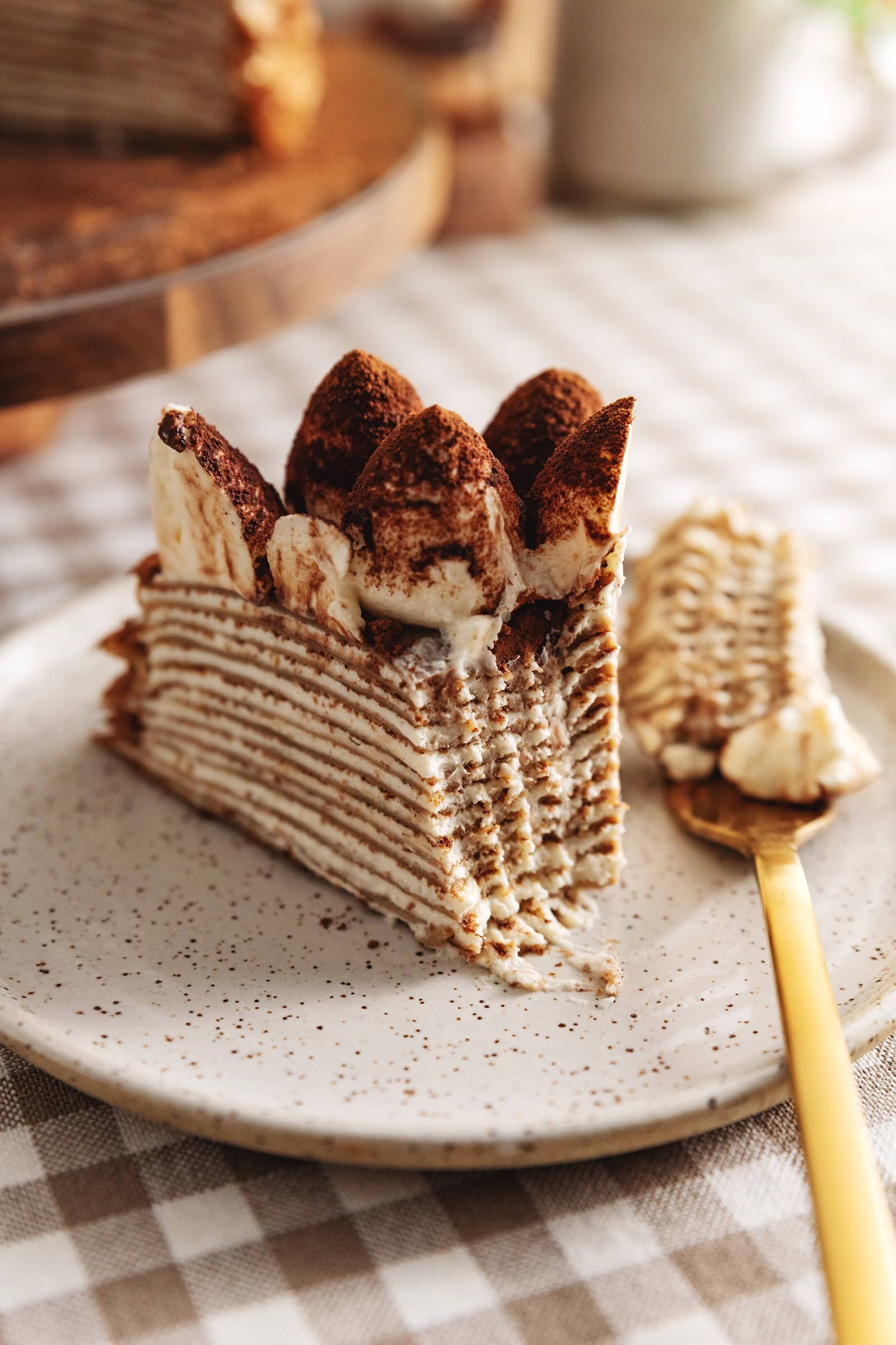 A slice of tiramisu crepe cake on a plate with a forkful taken out of it and the fork laying next to it.