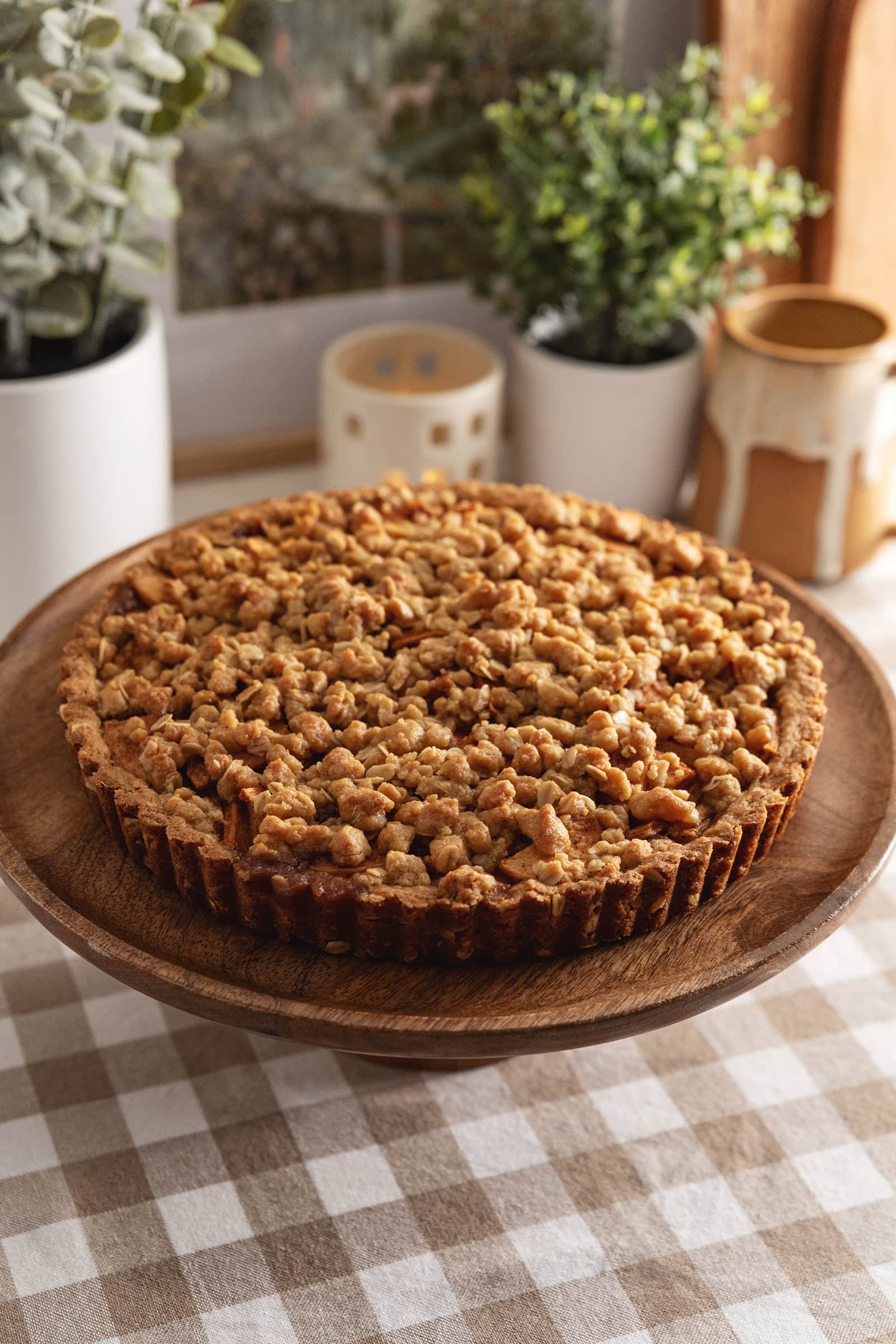 An apple crumble tart on a wooden cake stand.