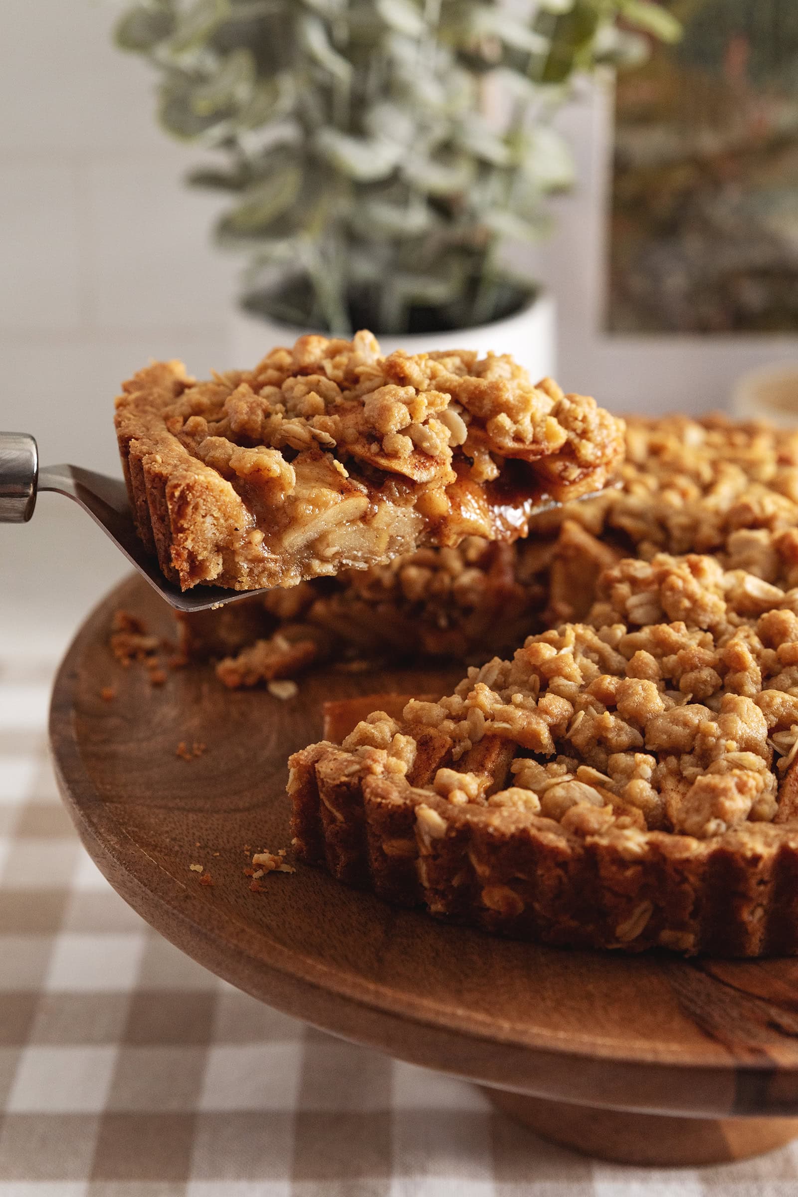 A slice of apple crumble tart being lifted above the rest of the tart with a cake server to show the apples inside.
