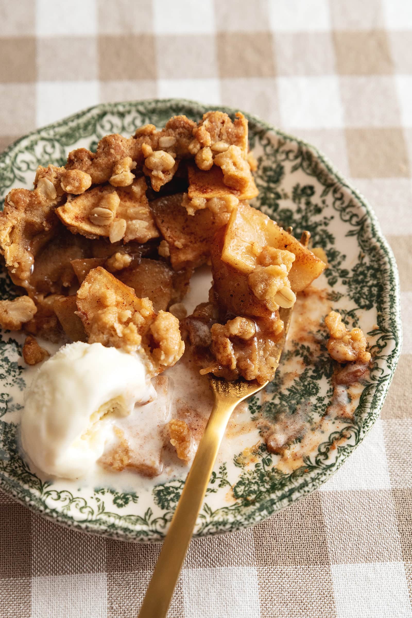 A plate of a half eaten slice of apple crumble tart and melted ice cream with a fork.