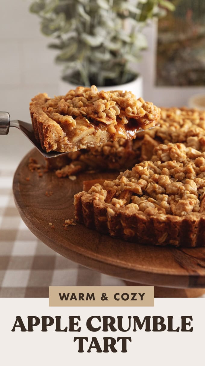 A slice of apple crumble tart being lifted above the rest of the tart with a cake server to show the apples inside.