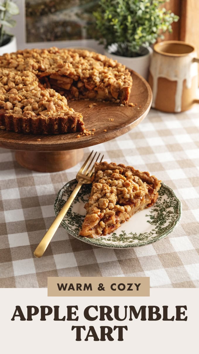 A slice of apple crumble tart on a plate in front of the rest of the tart on a kitchen counter.